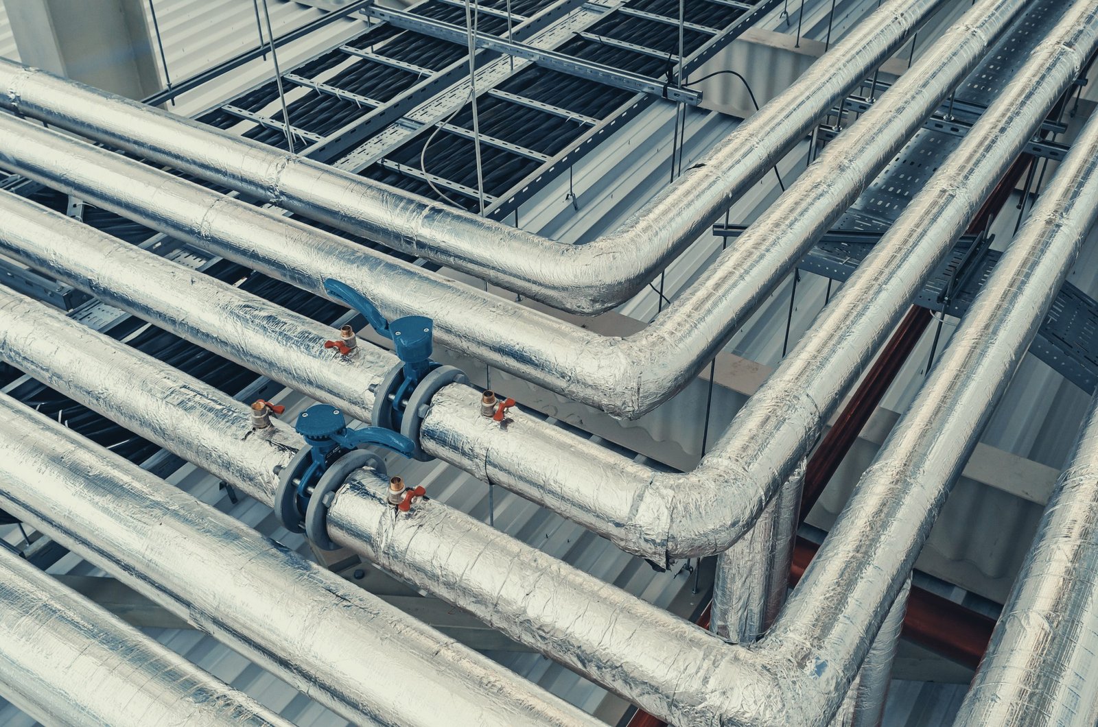 Metal pipes mounted under ceiling are covered with thermal insulation at modern production plant
